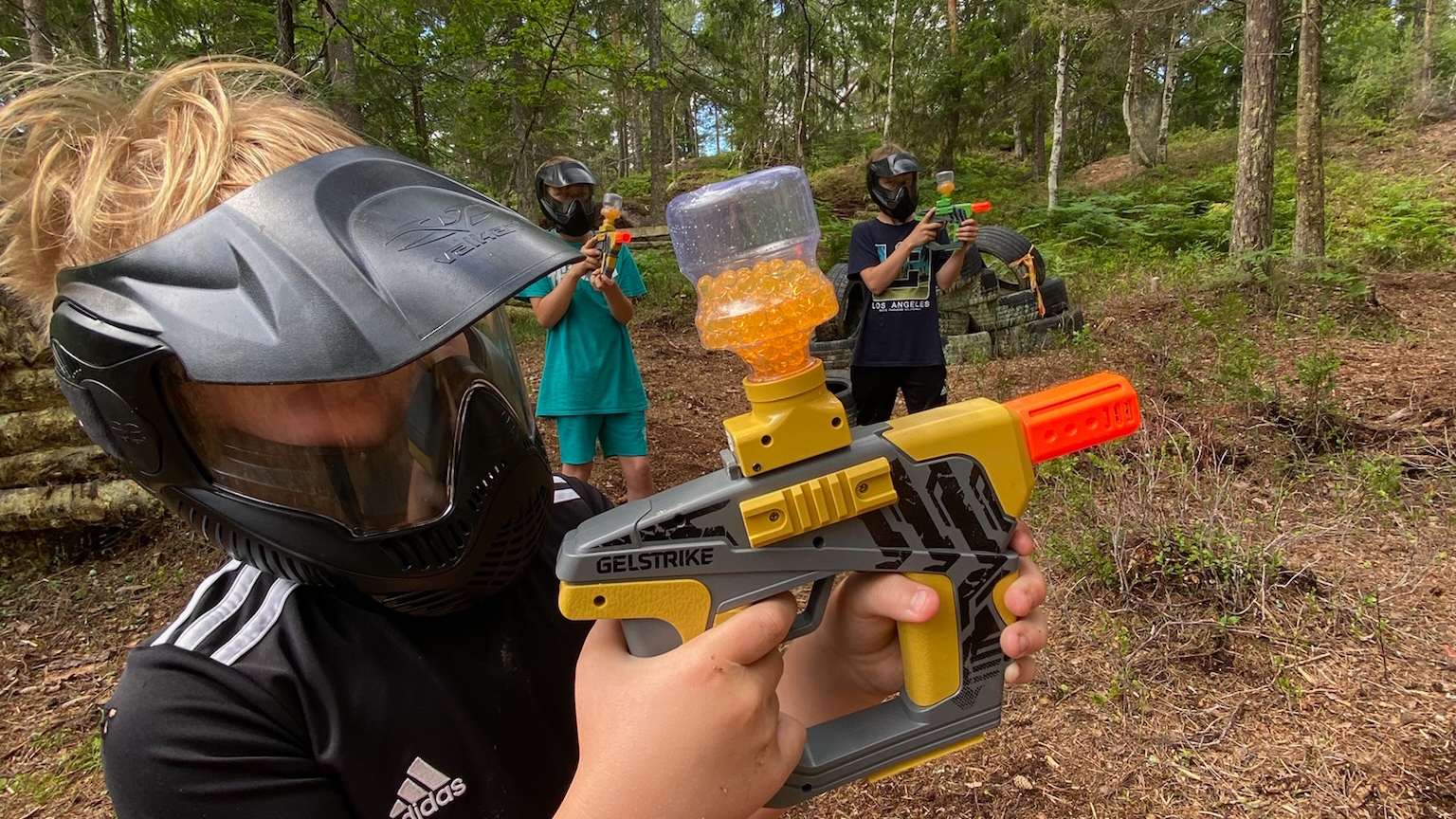 Barn som spelar splashball i skogen med skyddsmasker.